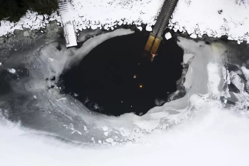 Two persons swimming big hole in the ice