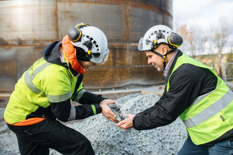 Two persons handling soapstone next to the Sand Battery.