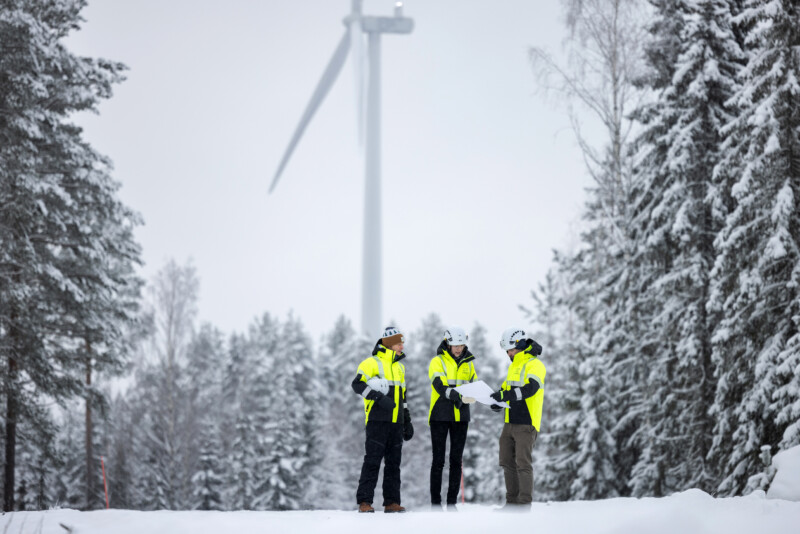 Three persons making plans. Wind turbine in the background.